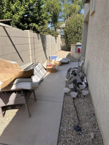 Outdoor furniture cushions, boxes, and miscellaneous junk piled in a side yard for removal by HD Junk Removal in Gilbert, AZ