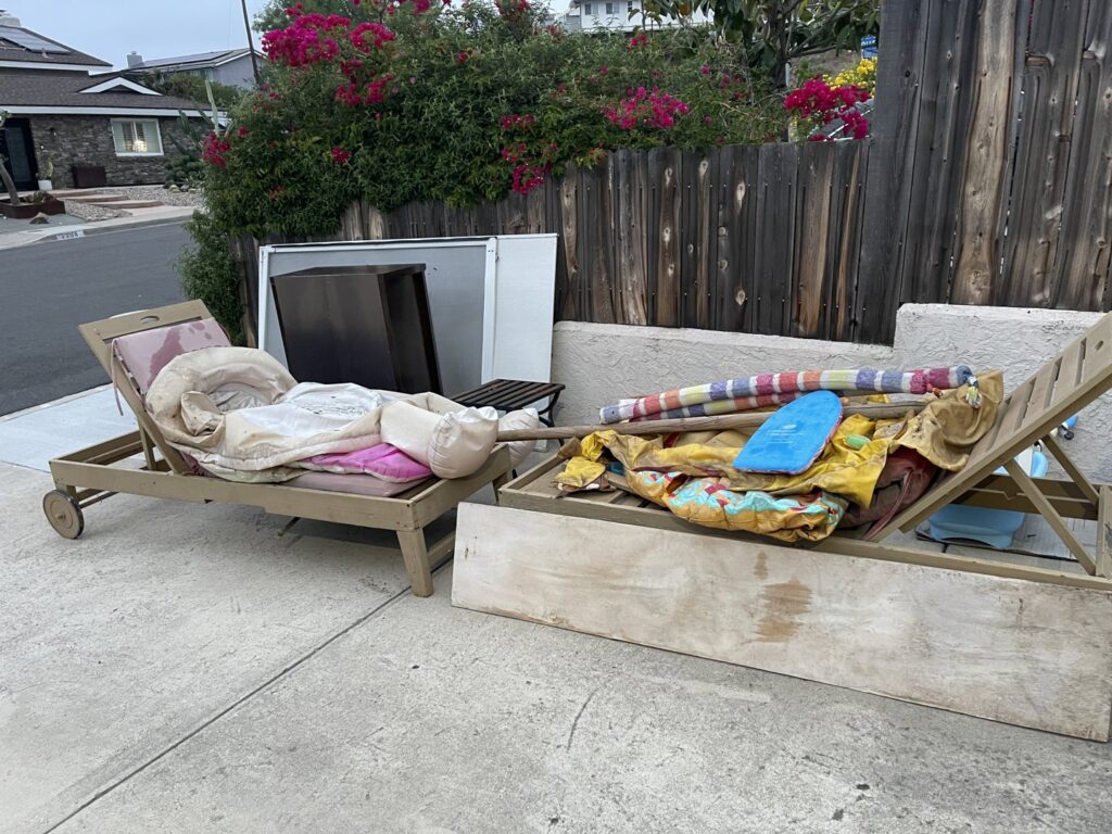 Old outdoor lounge chairs and other items placed on a driveway for junk removal by Gabriel's Hauling & Junk Removal Services in San Diego, CA.