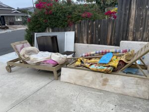 Old outdoor lounge chairs and other items placed on a driveway for junk removal by Gabriel's Hauling & Junk Removal Services in San Diego, CA.