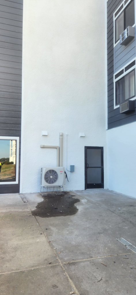 An outdoor HVAC unit with piping and a wet spot on the concrete, indicating potential maintenance or repair by Rocksolid Construction in Star Prairie, WI.
