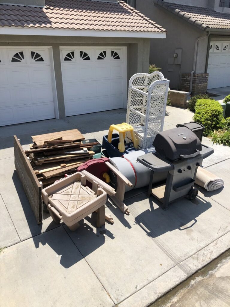 A pile of outdoor furniture, pallets, and a grill on a driveway for junk removal by The Junk Gentlemen in Anaheim, CA.