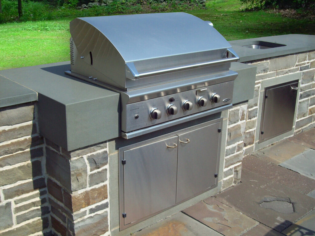 An outdoor kitchen featuring a built-in stainless steel grill and a custom stone base by Adam Ross Cut Stone in Albany, NY.