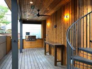 A spacious outdoor kitchen and deck area with a built-in grill, ceiling fan, and spiral staircase by Kaleidoscope Design Build in Houston, TX.