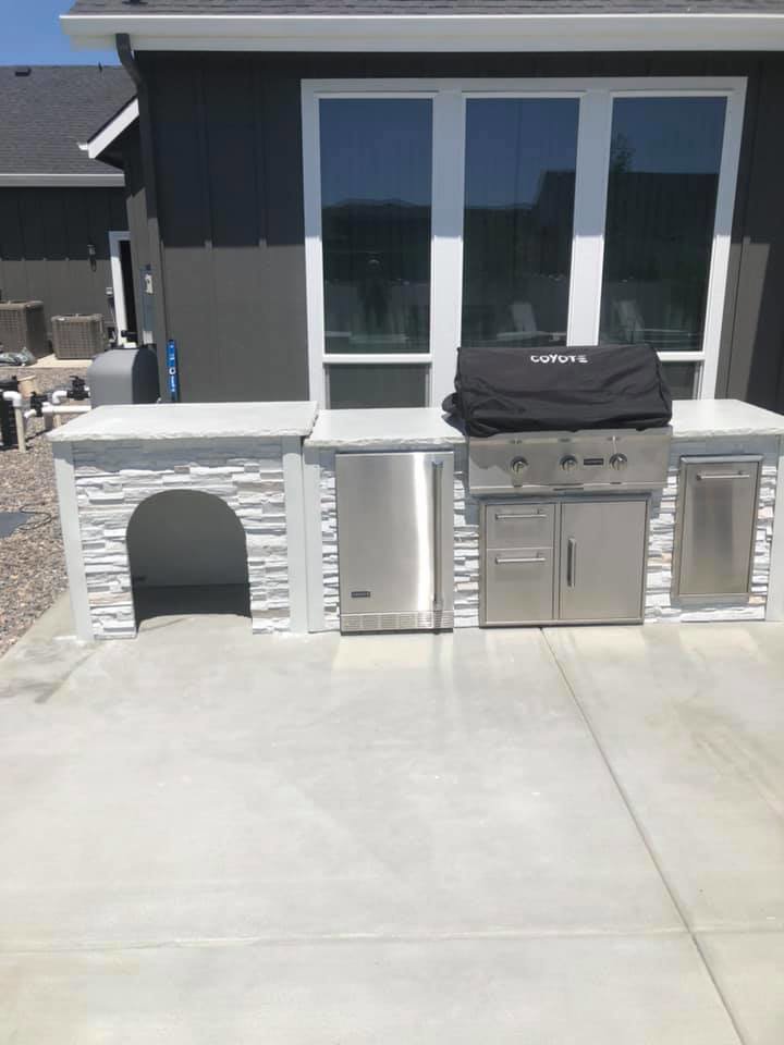 A custom outdoor kitchen with a built-in grill and refrigerator, constructed by The Huckleberry Handyman in Meridian, ID.