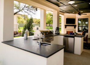 A completed outdoor kitchen featuring a built-in grill, sink, and dark countertops by AAA Countertops in Austin, TX.