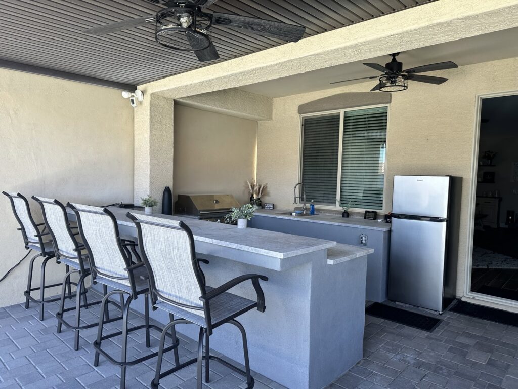 A newly installed outdoor kitchen and bar area with ceiling fans and string lights, completed by Fair & Square Pools in Chandler, AZ