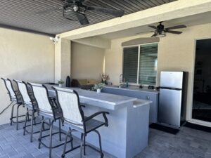 A newly installed outdoor kitchen and bar area with ceiling fans and string lights, completed by Fair & Square Pools in Chandler, AZ