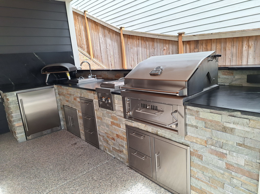 A newly installed outdoor kitchen with stone veneer and built-in grill by Eagle Outdoor Living LLC in Freeland, WA.