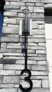 An outdoor light fixture and house number '3' installed on a stone wall by Elevate Design + Build in Philomath, OR.