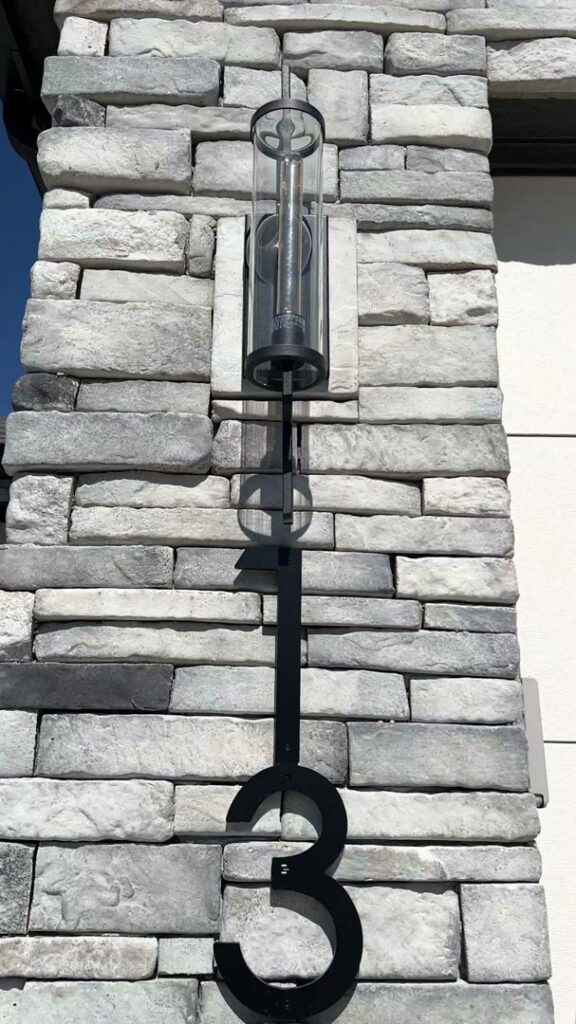 An outdoor light fixture and house number '3' installed on a stone wall by Elevate Design + Build in Philomath, OR.