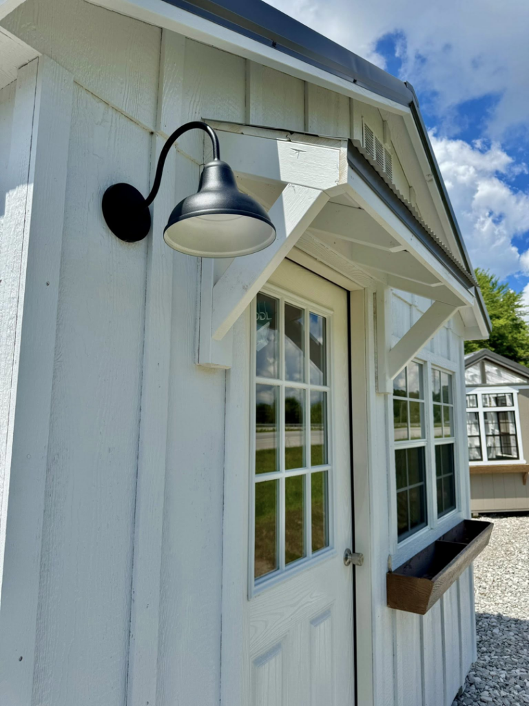 An outdoor light fixture professionally installed on a white shed by Backyard and Beyond in London, KY.
