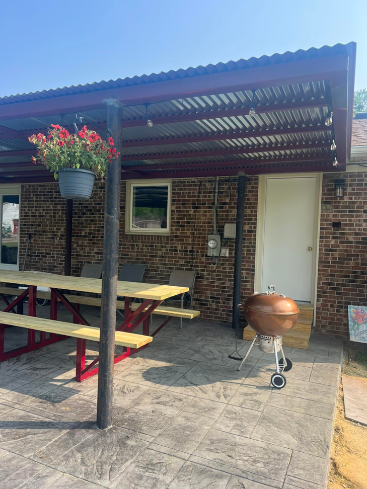 An outdoor metal patio cover with string lights installed over a stamped concrete area by Boyce Welding, LLC in Courtland, VA.