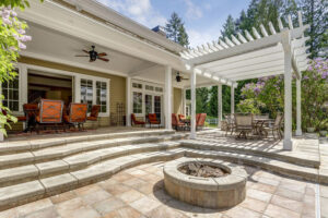 An outdoor patio with a stone fire pit and a white pergola by St. Charles Deck in St. Charles, MO