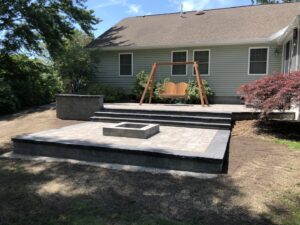 An outdoor patio with paver stones, retaining walls, and a built-in fire pit constructed by Rock Solid Construction in Rochester, NY