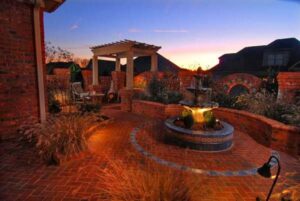 An elegant outdoor patio with a lighted fountain and brickwork at dusk by Rothrock Renovation & Remodeling in Winston-Salem, NC