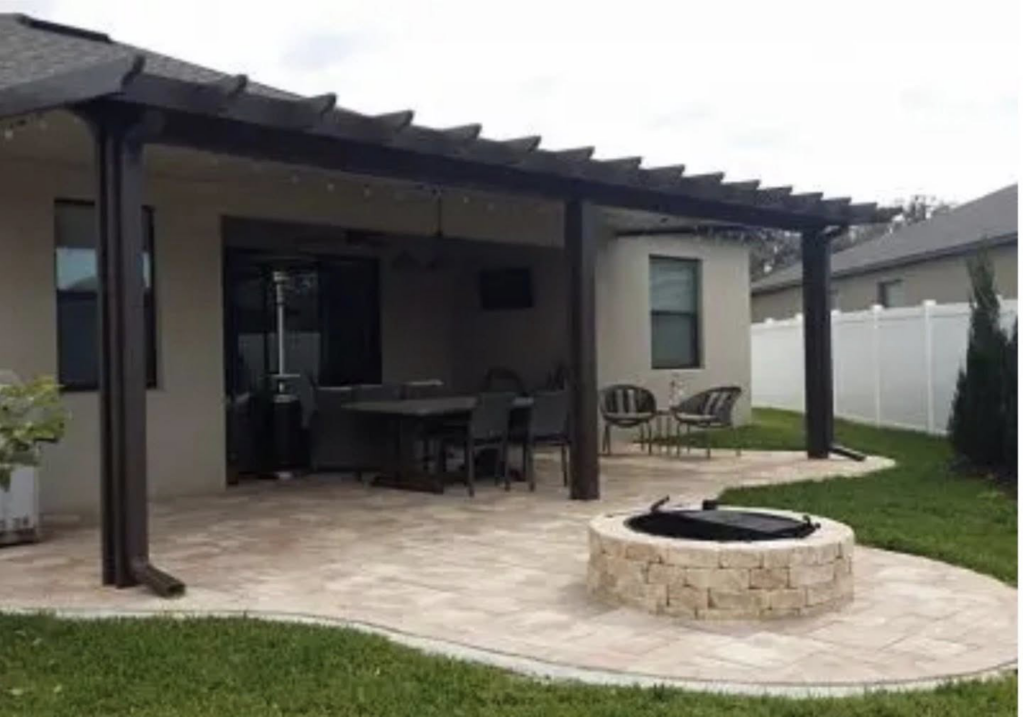 A beautiful outdoor patio with a wooden pergola, paved area, and stone fire pit, constructed by Cover Works in Luling, LA.