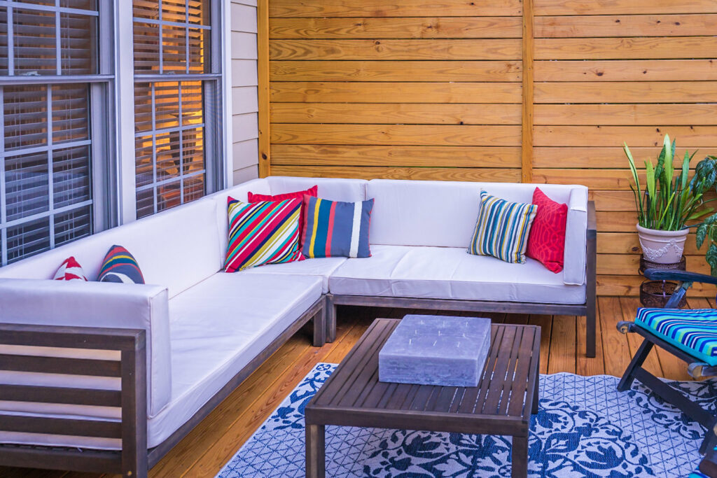 An outdoor patio with a comfortable sectional sofa and a wooden privacy wall by Constructive Design Group in Raleigh, NC