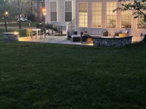 A newly installed outdoor paver patio with a fire pit and stone retaining walls, lit up at night by Landscape By Today in Bowie, MD.