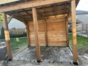 A newly constructed wooden pergola with a metal roof and stone patio by K-Way's Handyman Services in Lincoln, NE