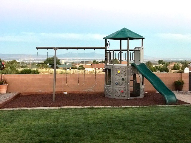 A newly installed outdoor playset with swings and a slide in a backyard, showcasing assembly services by The ABQ Handyman in Albuquerque, NM.
