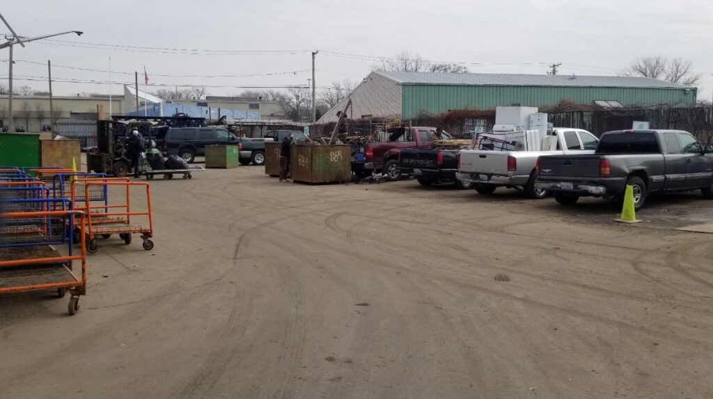 An outdoor recycling yard with trucks, dumpsters, and workers at Get Green Recycling Co. in Aurora, IL.