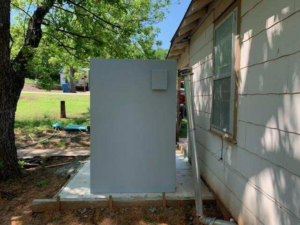 An outdoor safe room storm shelter installed next to a house on a concrete pad by Taylor Storm Shelters in Stillwater, OK.
