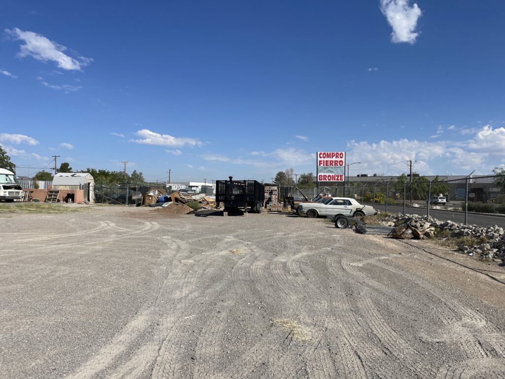 An outdoor scrap yard with various piles of junk, a trailer, and an old car at FL Scrap in El Paso, TX, for general junk removal.