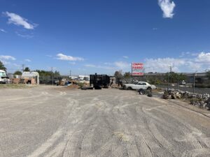 An outdoor scrap yard with various piles of junk, a trailer, and an old car at FL Scrap in El Paso, TX, for general junk removal.