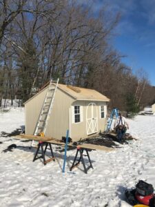 An outdoor shed under construction or renovation in a snowy landscape, with a worker and tools, by Home pro handyman llc in Olathe, KS