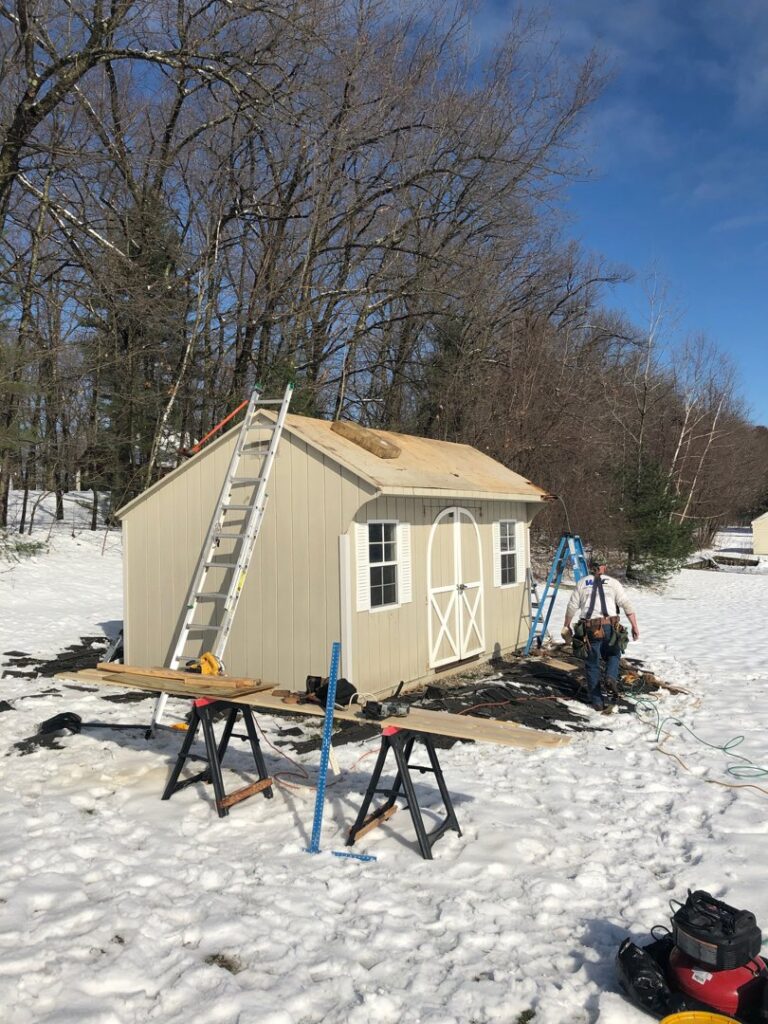 An outdoor shed under construction or renovation in a snowy landscape, with a worker and tools, by Home pro handyman llc in Olathe, KS