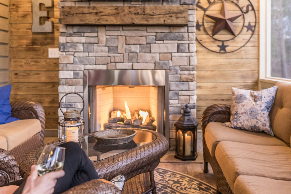 An inviting outdoor stone fireplace with a wooden mantel and comfortable seating by Constructive Design Group in Raleigh, NC