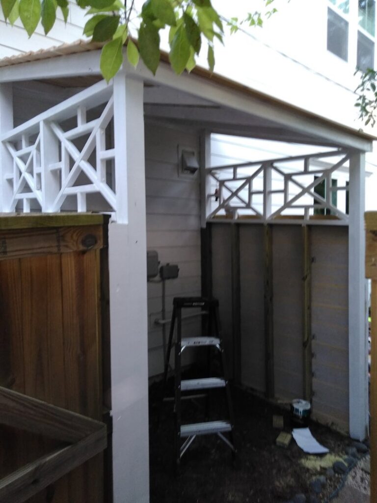 A handyman painting an outdoor utility enclosure or shed with decorative railing for Holy City Remodel in North Charleston, SC.