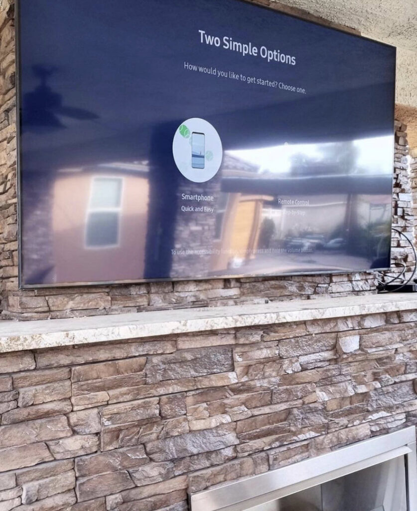 An outdoor TV mounted on a stone wall, displaying a setup screen, installed by Tech Handy-Las Vegas in North Las Vegas, NV.