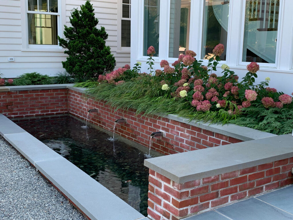 An elegant outdoor water feature with brickwork and lush plants installed by Santoro Home Improvements in Wallingford, CT.