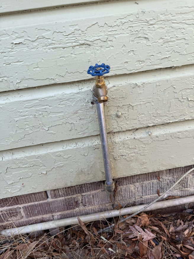 An outdoor water spigot with a blue handle installed on the exterior of a house, representing plumbing services from Helms Plumbing and Drains in Charlotte, NC.
