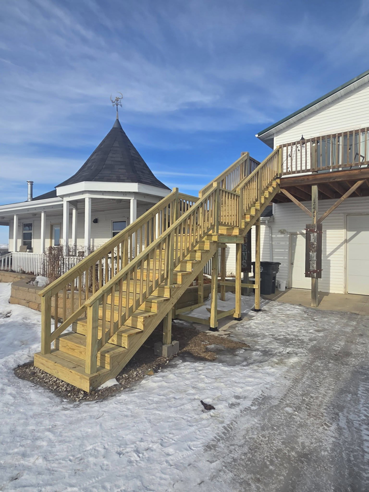 A newly constructed outdoor wooden deck and staircase leading to a house by Joe Norton's Handyman Service in Williston, ND.