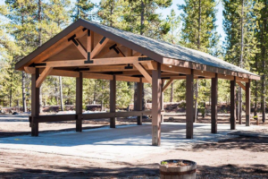 A newly constructed outdoor wooden pavilion in a forest setting by Winch Construction in Bend, OR.
