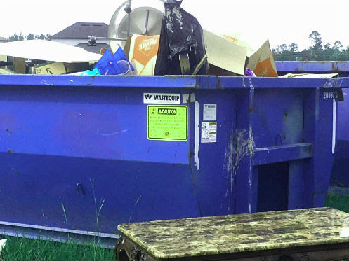 An overflowing blue dumpster filled with various trash and boxes, indicating a large-scale junk removal job by Trashouts Junk Removal in Pembroke Pines, FL.