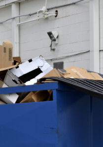 A blue commercial dumpster overflowing with cardboard boxes, demonstrating junk removal by RBS Sanitation Inc. in Tea, SD.