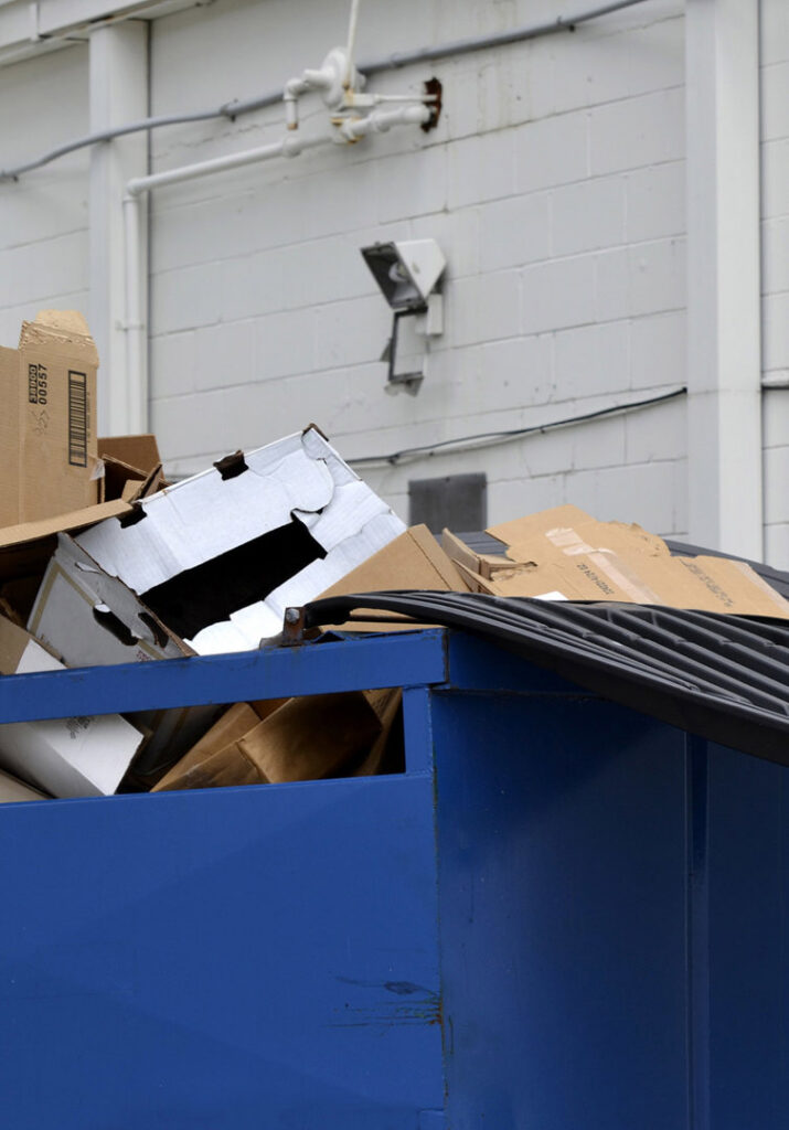 A blue commercial dumpster overflowing with cardboard boxes, demonstrating junk removal by RBS Sanitation Inc. in Tea, SD.