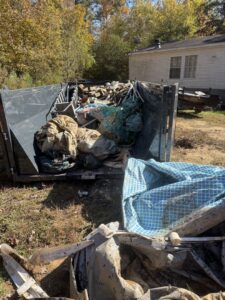 An overflowing roll-off dump container filled with various debris and junk, showcasing a completed removal job by Lewis Outdoor Services LLC in Augusta, GA.