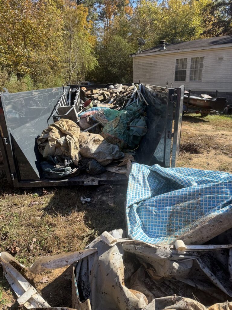 An overflowing roll-off dump container filled with various debris and junk, showcasing a completed removal job by Lewis Outdoor Services LLC in Augusta, GA.