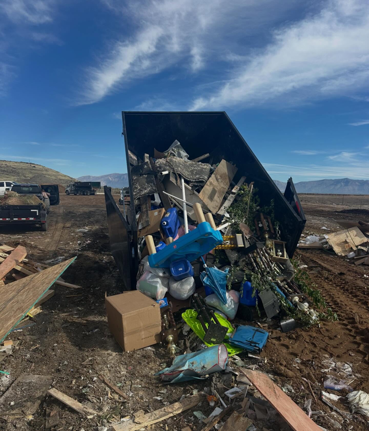 An overflowing TrashDash dumpster filled with various debris at a demolition or construction site in West Haven, UT.