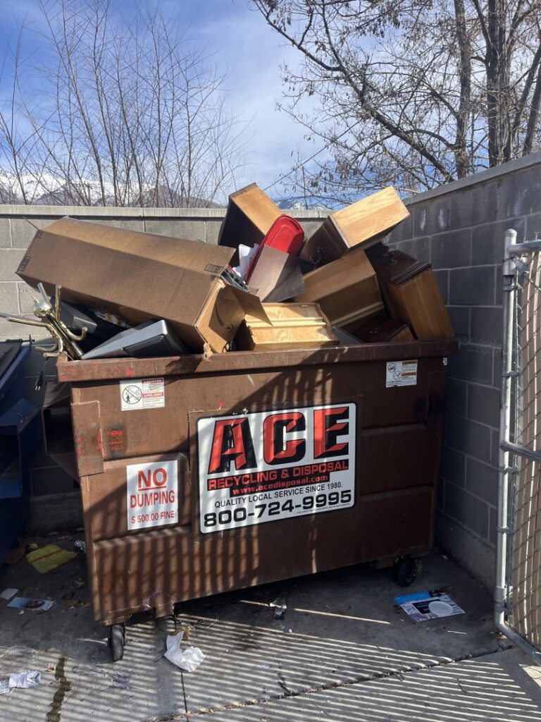 An overflowing brown dumpster filled with various household and furniture junk, representing a typical job for Junk Solutions in Ogden, UT.