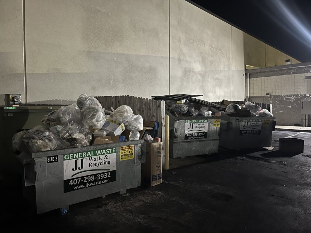 Three overflowing dumpsters filled with general waste at night, ready for pickup by JJ's Waste & Recycling in Orlando, FL.