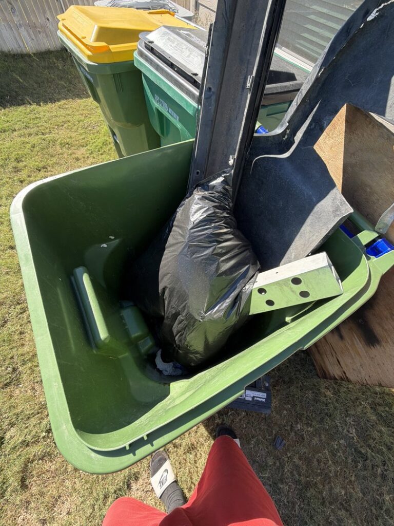 An overflowing green trash bin filled with various junk items, ready for pickup by Junk Out Boyz LLC in Georgetown, TX.