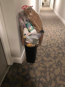 An overflowing trash bin with a clear bag of household junk in a hallway, collected by Elite Valet Trash in Apex, NC.