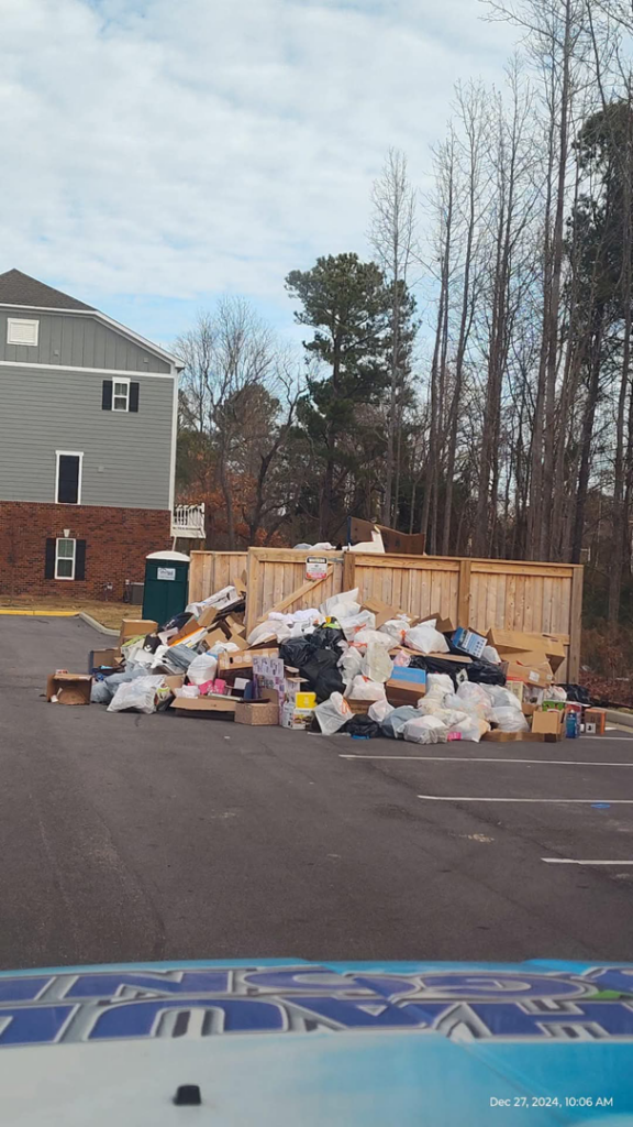 An overflowing pile of junk and debris next to a wooden enclosure at an apartment complex, representing a common junk removal job for Haul Gone 757 in Chesapeake, VA.