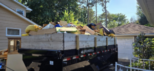 An overflowing roll-off dumpster filled with various junk items at a residential property by At Ease Dumpsters and Junk Removal in Welch, MN.
