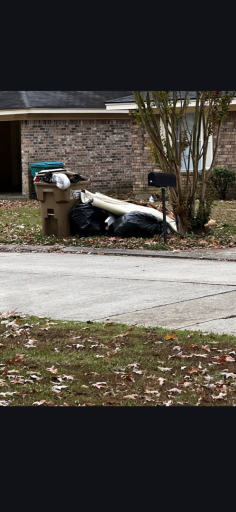An overflowing trash can filled with bags and junk next to a residential house, awaiting removal by Tote Junk Removal & Demo, LLC in Monroe, LA.